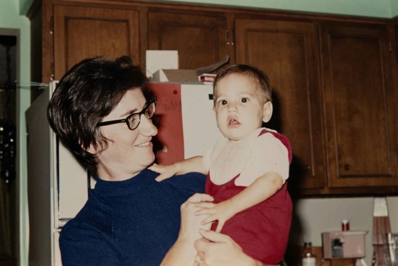 a woman is holding a young baby in the kitchen