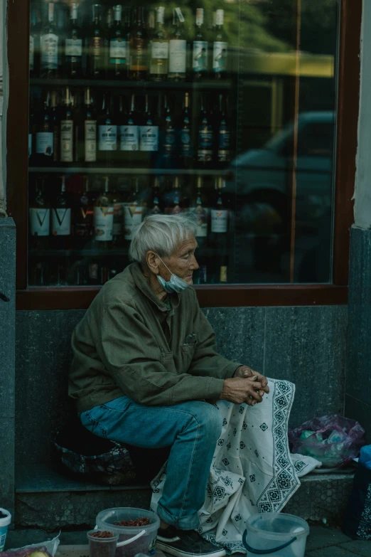 an old man sits on a corner by some bottles