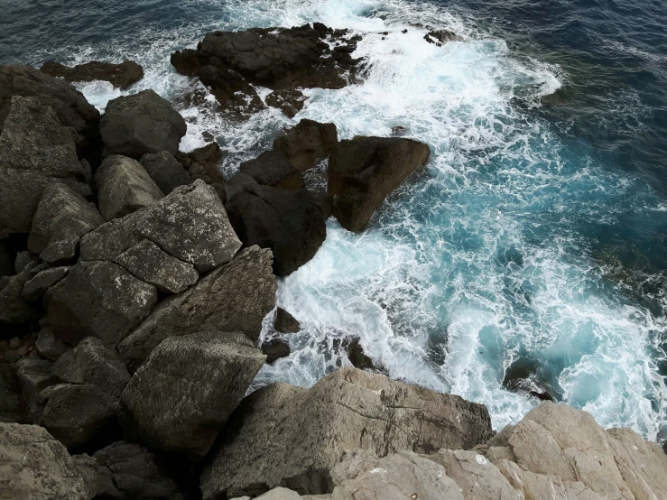 a wave rolls into the shore near some rocks