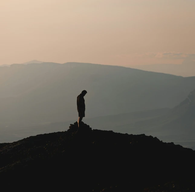 person standing on top of a hill gazing at the distant mountain