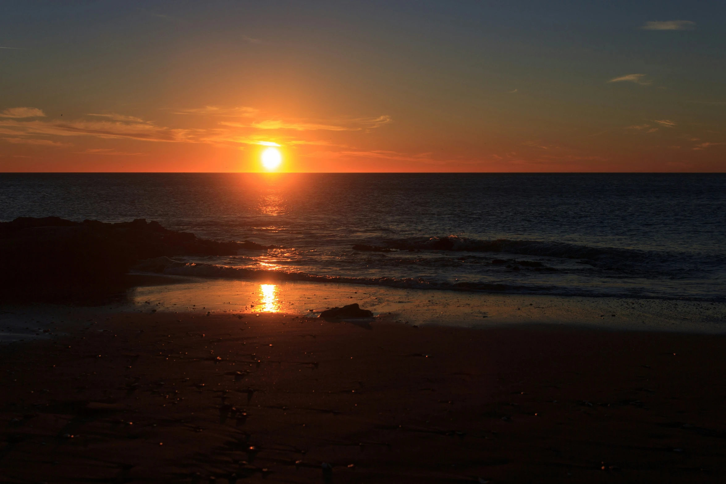 the sun rising over water with seaweed on shore