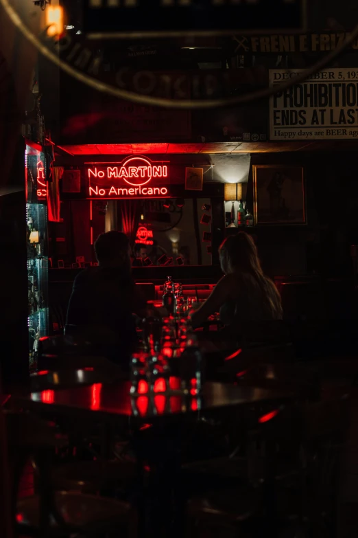 two people sitting at a table under a red neon sign