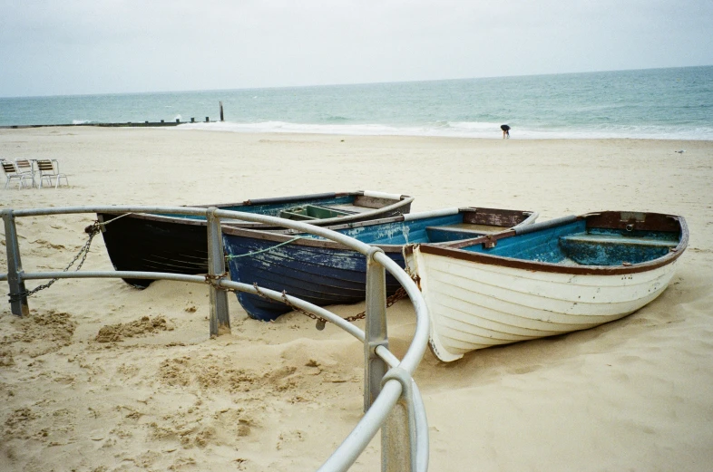 two boats in the sand next to an old metal railing