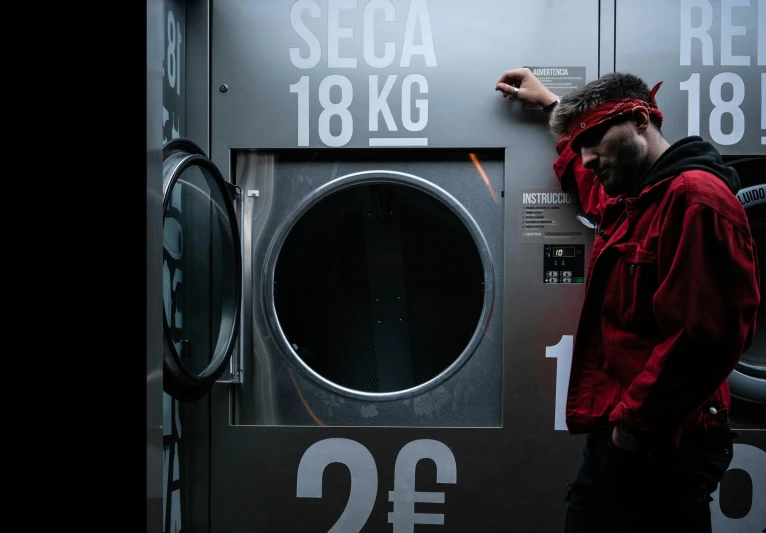 a man in a red jacket puts an item into a metal washing machine