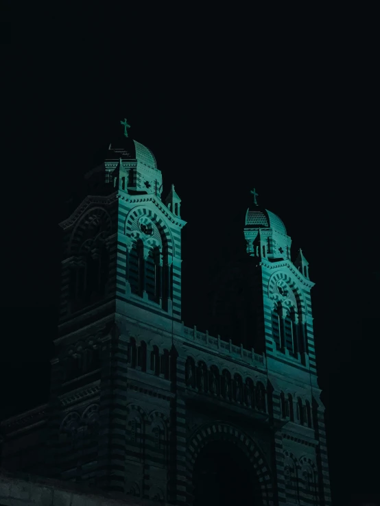 two towers with clocks at the top lit up green in the dark