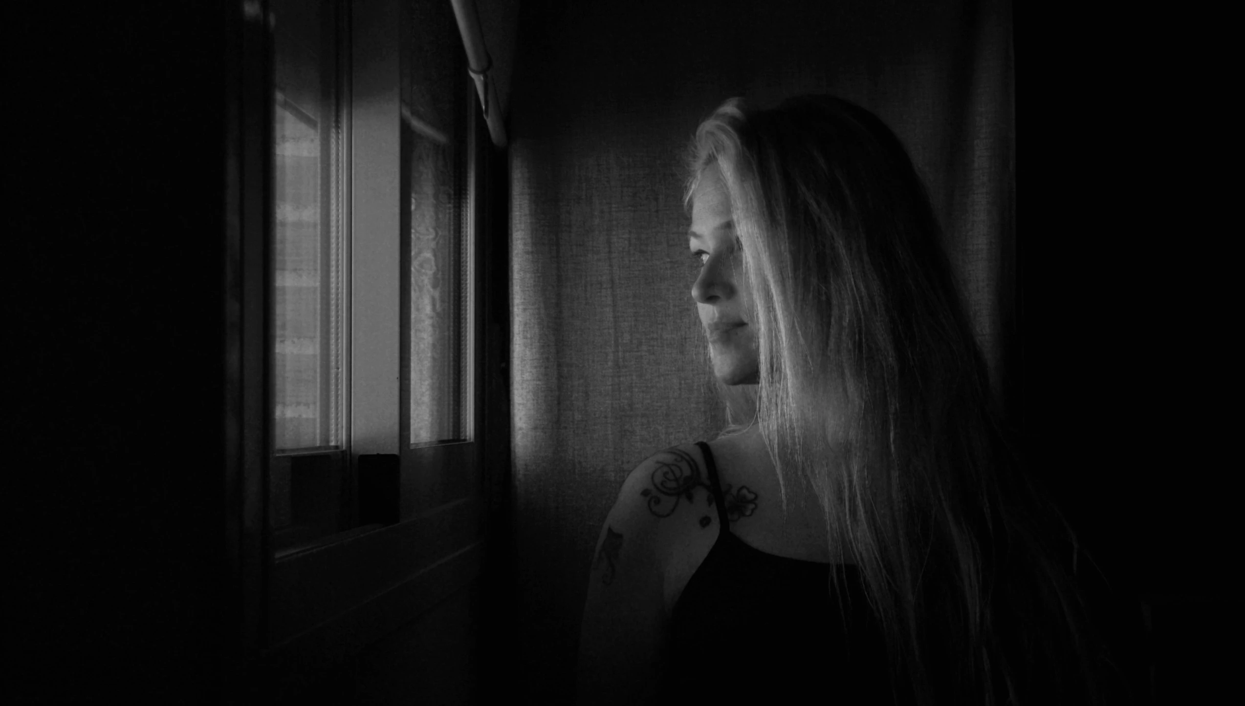 black and white pograph of girl staring out window at dark