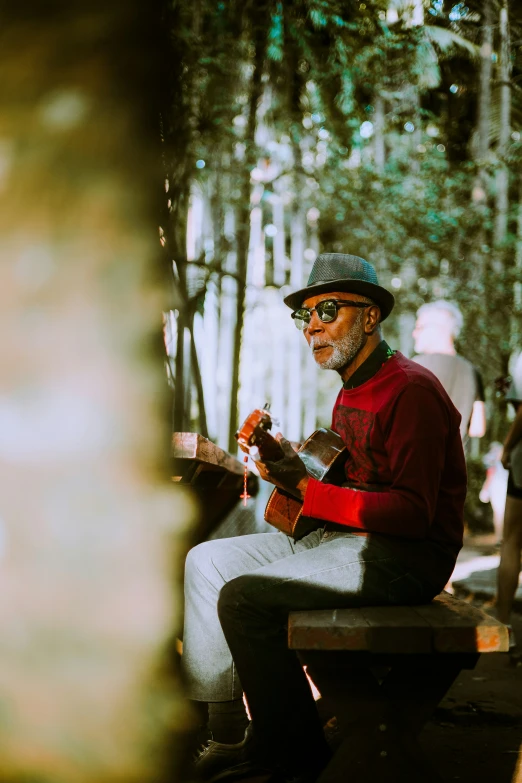 a man that is sitting on a bench with a guitar