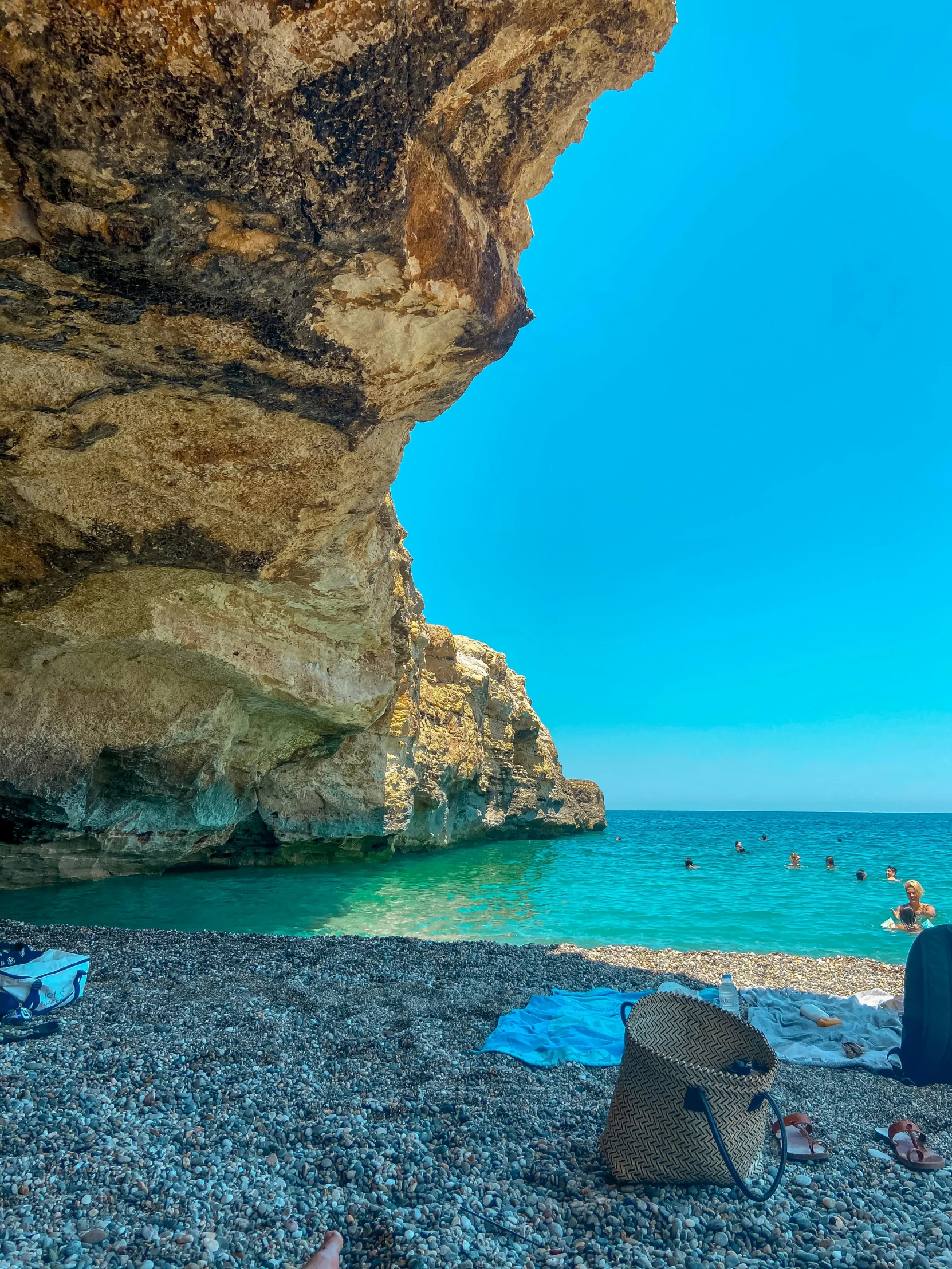 a person is sitting on the beach under a rock