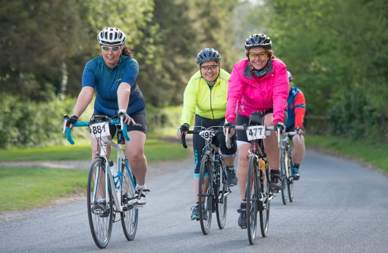 three people are riding bicycles down a rural road