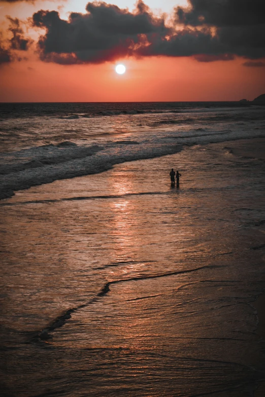 two people are wading in the water at sunset