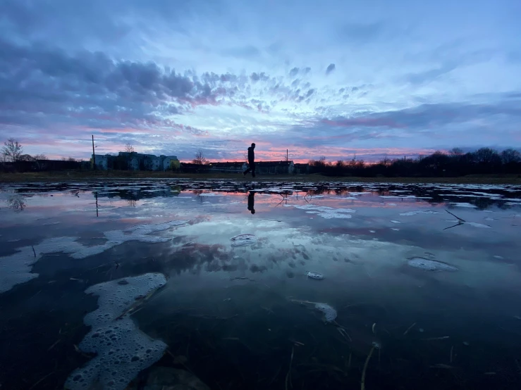 a purple sunset reflects in the water of a pool of icy ice