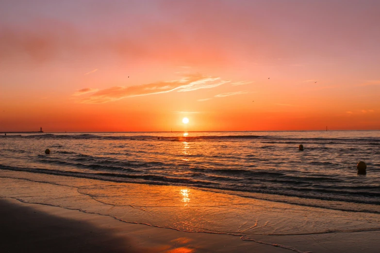 the sun sets over the water on a beach