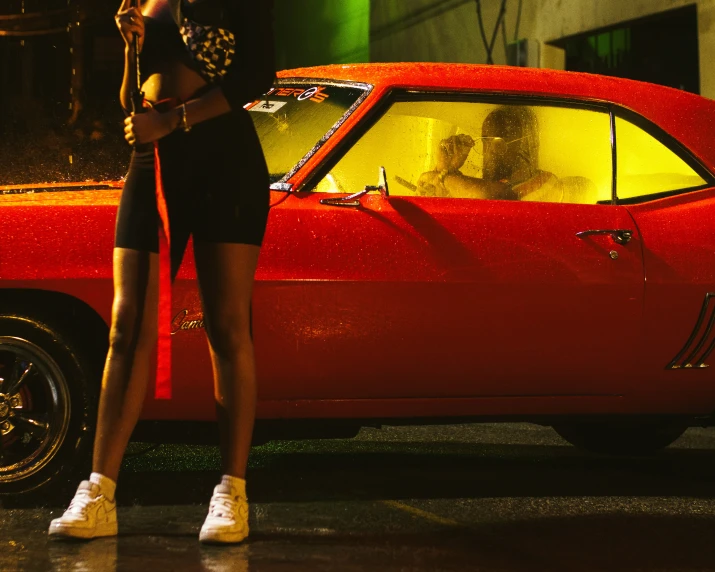 a woman leaning against a red car on the street