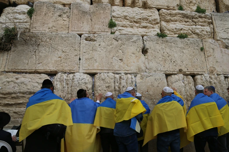 men in bright robes pray near a rock formation