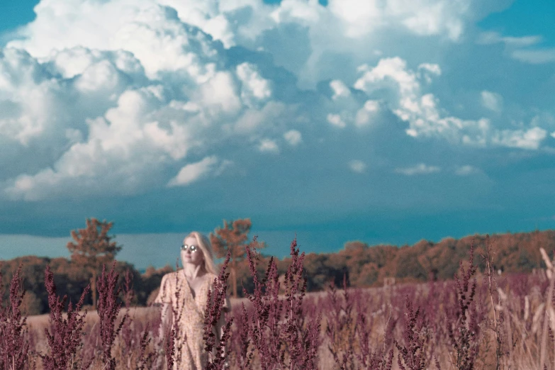 a creepy looking woman in a field near clouds