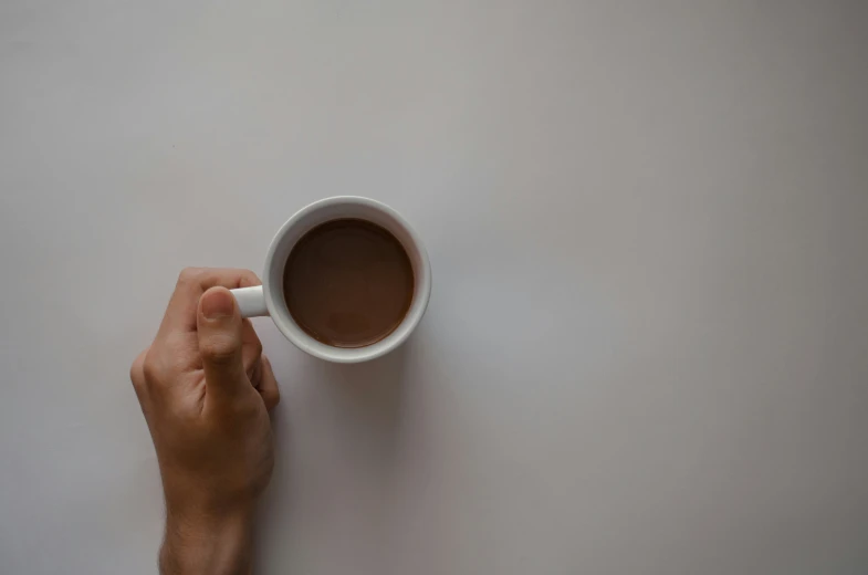 a hand on the side of a wall writing on a coffee cup