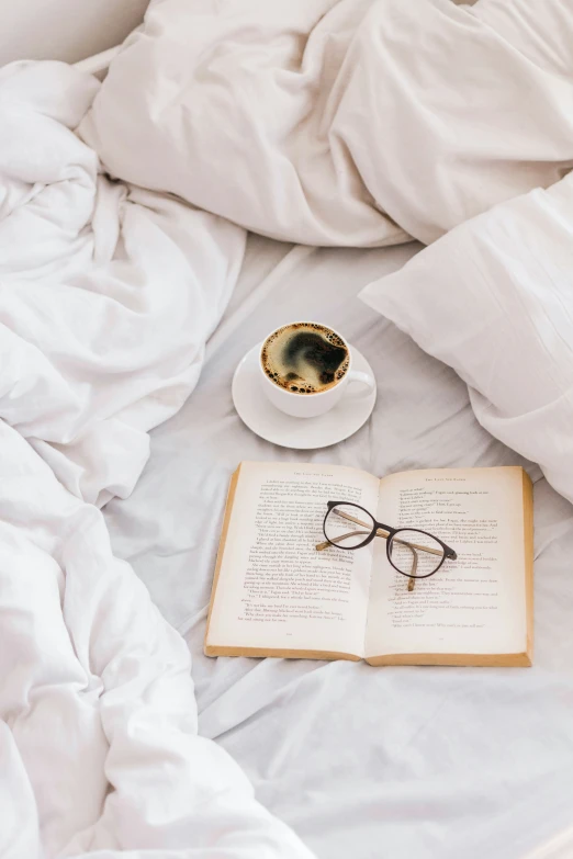 an open book and eyeglasses sit on a bed