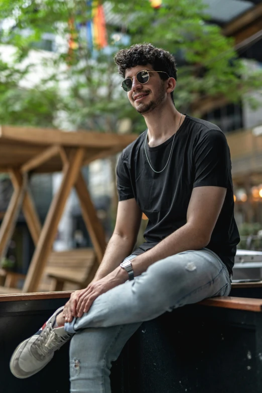 man in sunglasses sitting on wall in a city