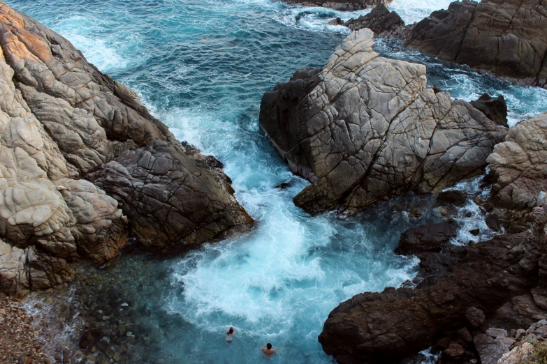 people wading in a pool between two large rocks