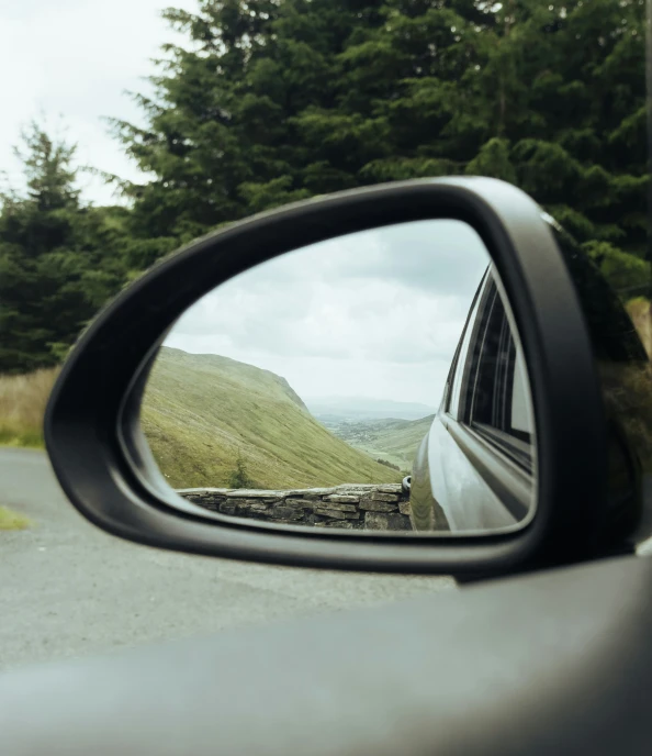 a rear view mirror with a side view of mountains and trees