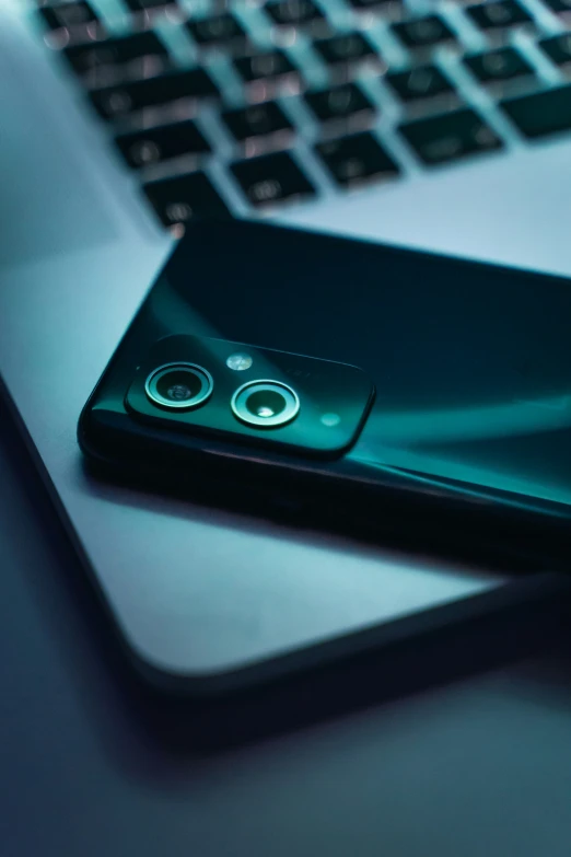 the rear of a green cell phone sits on top of a laptop