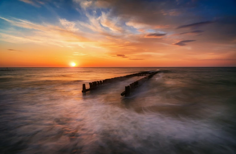 an ocean wave rolls in at a long pier