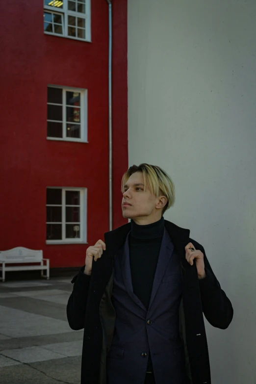 man in black jacket standing next to red building