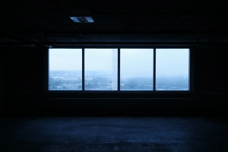 a dark room with two windows looking out at the city