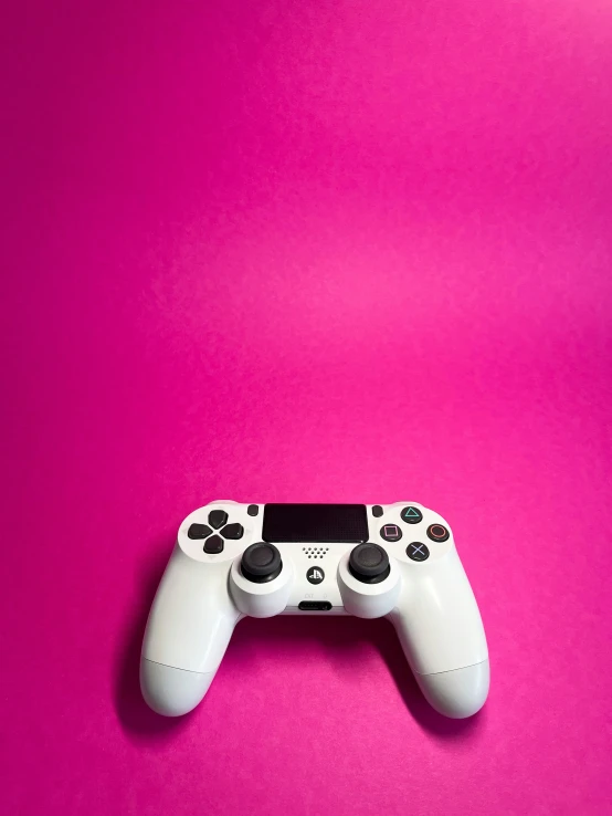 a white controller is on a pink surface