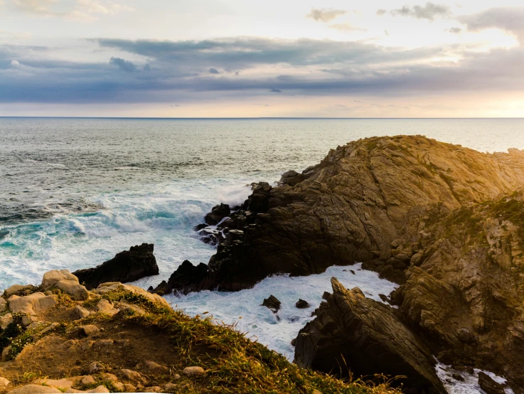 a large cliff overlooking the ocean under a cloudy sky