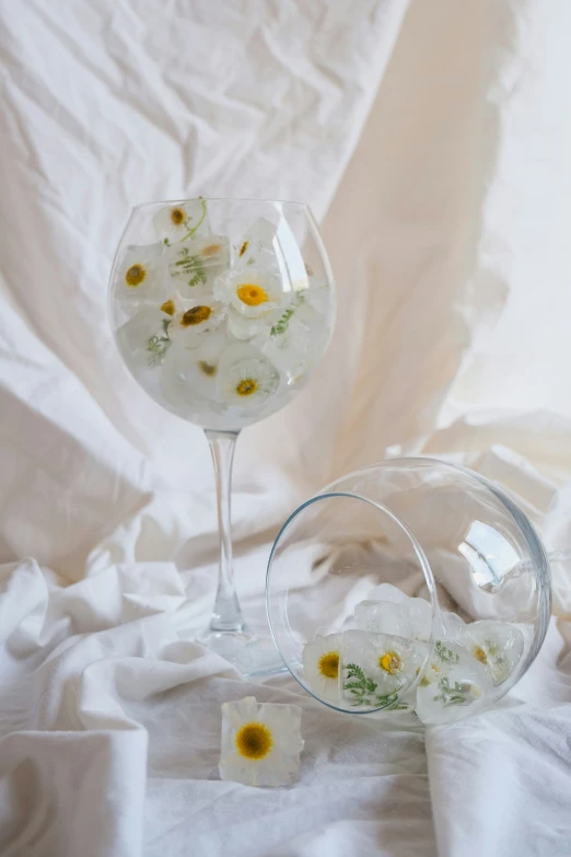 some flowers and petals are in a wine glass on a white cloth