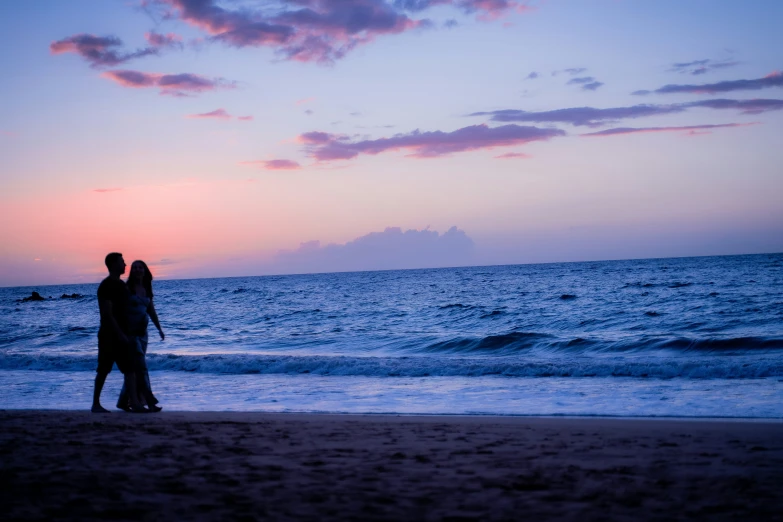 the silhouette of two people stand at sunset on the beach