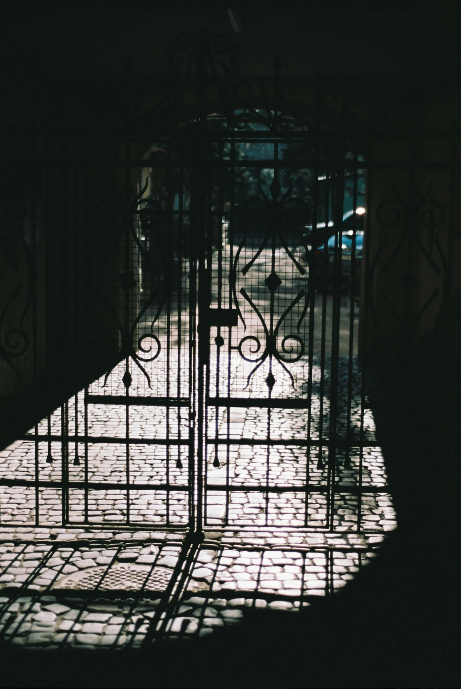 an iron gate opened to a building with people walking out the doors