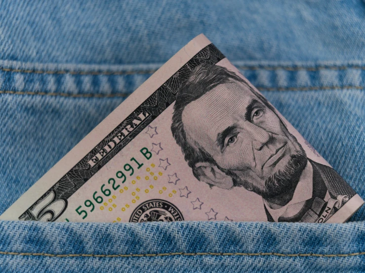 the back pocket of a pair of jeans showing an hundred dollar bill sticking out