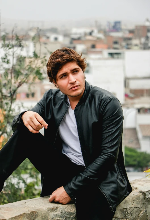 man wearing black outfit sitting with a city in background