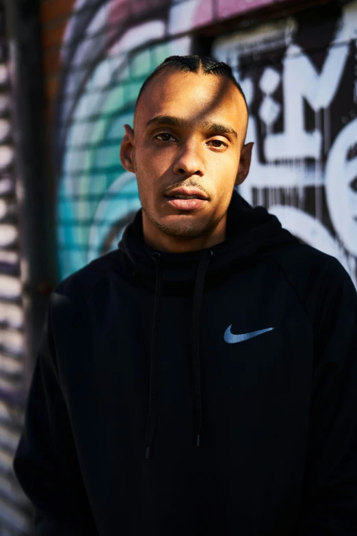 man in hooded sweatshirt posing by wall with graffiti