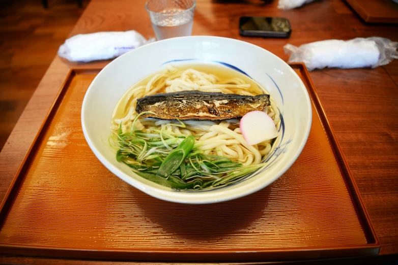 there is noodle soup with fried fish on it