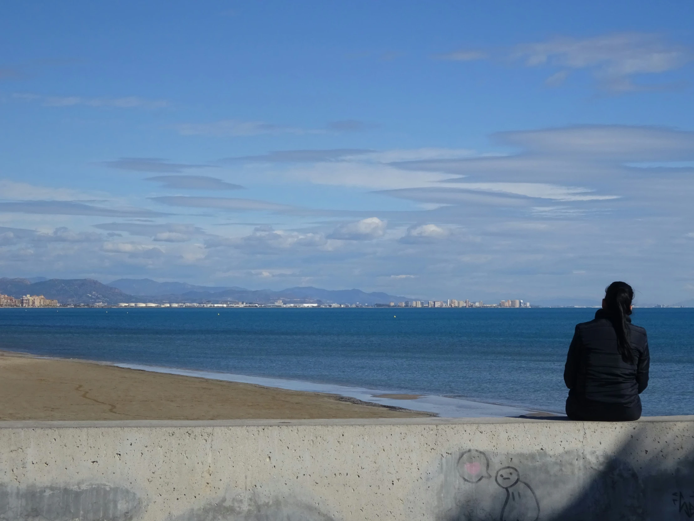 the man sits on a cement ledge looking out at the ocean