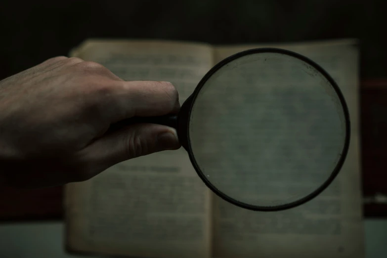 a hand holding a magnifying glass over an open book