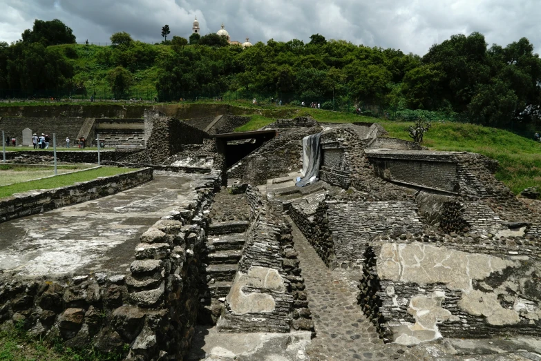 several ancient buildings in ruins with a green hill in the background