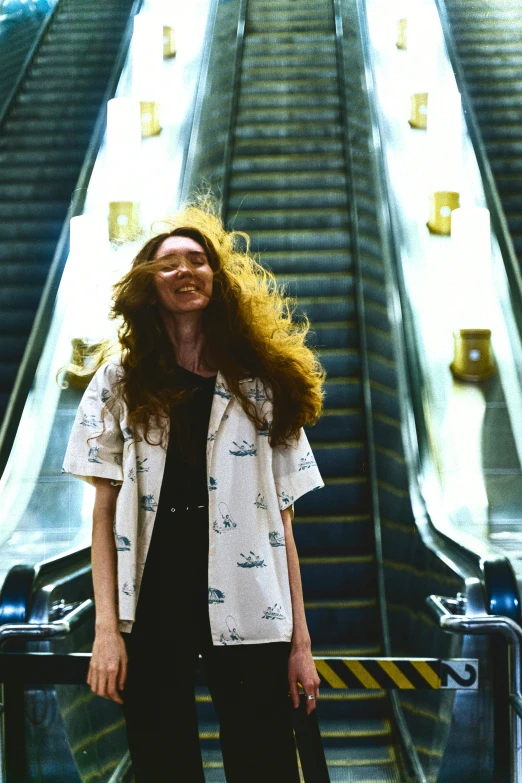 a woman is smiling and standing next to a moving staircase