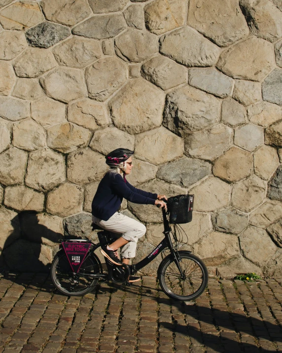 a  rides a bicycle in front of a stone wall