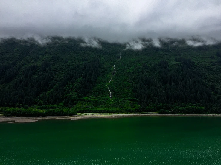 a green lake surrounded by wooded mountains on a cloudy day