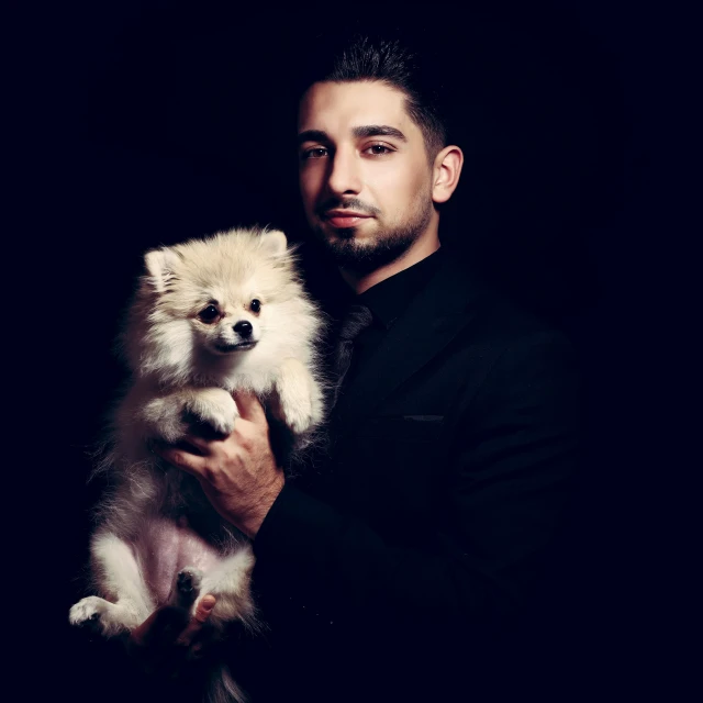 a man holding a white pomeranian puppy in his right arm