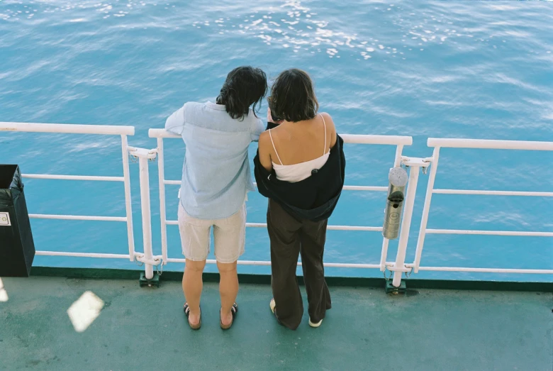 two people are looking over the railing to the water