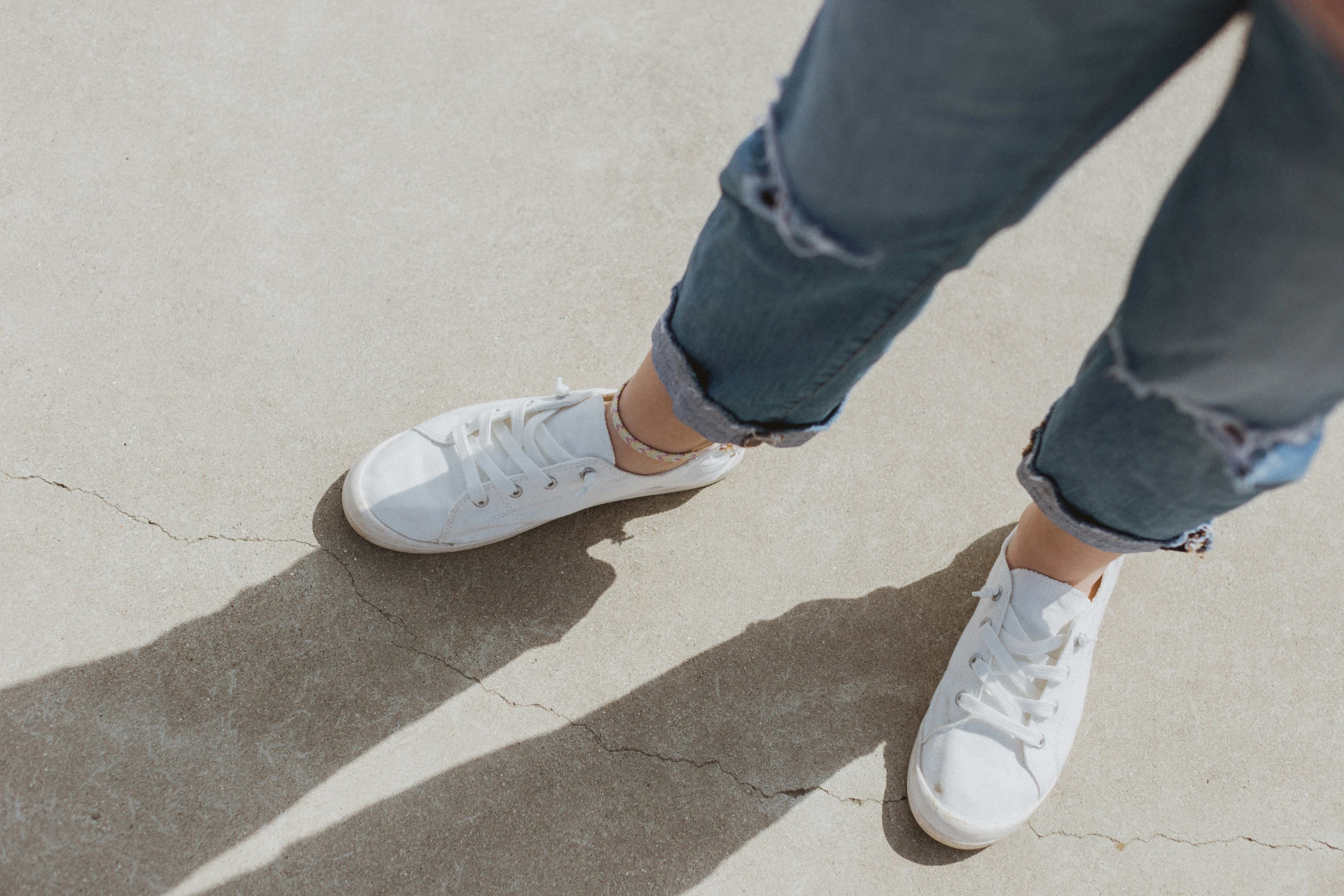 a person in ripped pants and sneakers standing on concrete