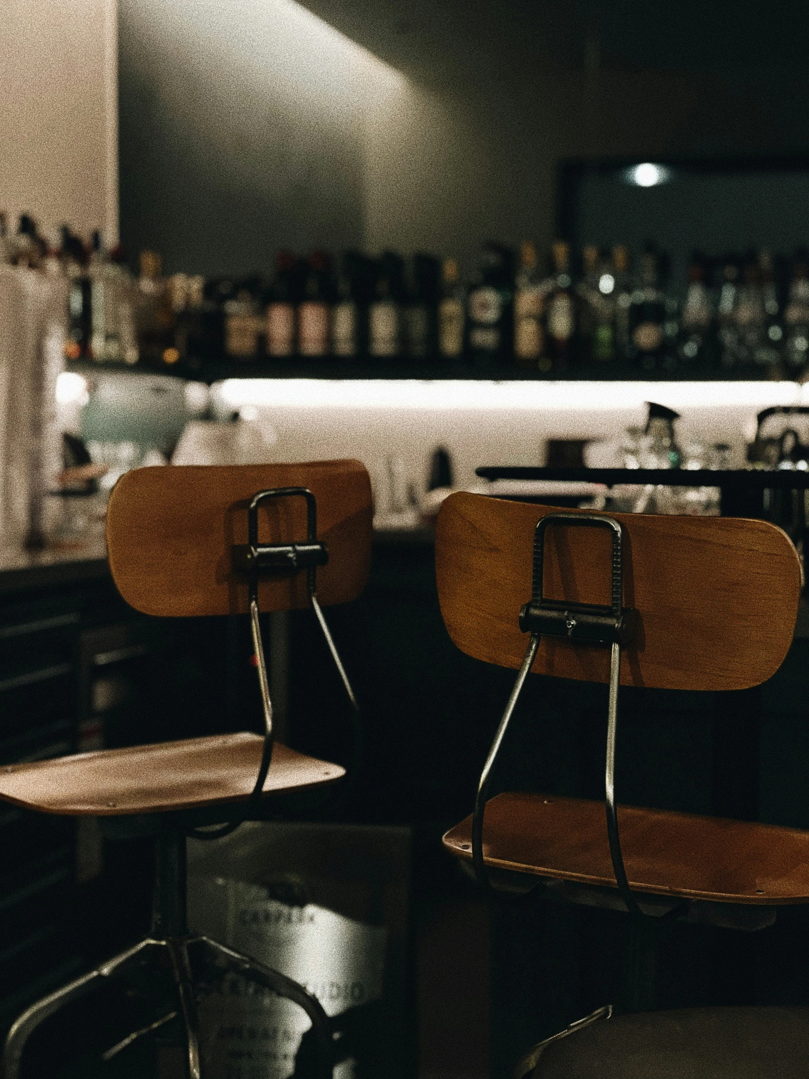 two chairs on a bar with some wine glasses on the back wall