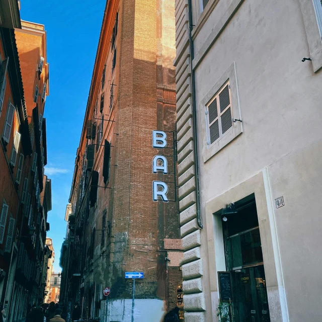 two tall buildings on one side and a bar sign on the other