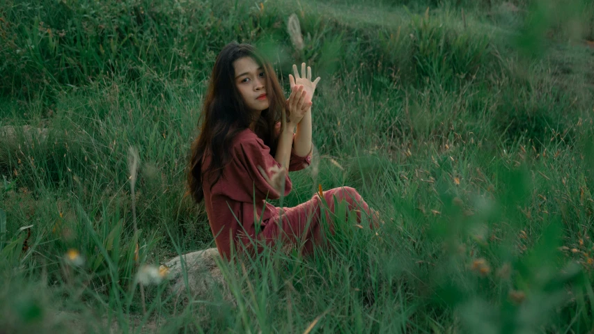 a woman sitting in a grassy field waving