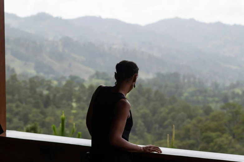 the woman standing outside of the window looks out at the mountains